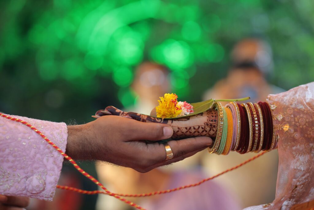 Close-up of hands in a traditional Indian wedding ritual with henna and vibrant bangles.