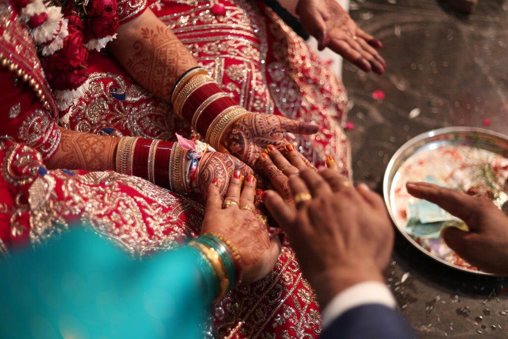 Close-up of hands with henna at a traditional wedding ceremony, showcasing cultural attire and jewelry.